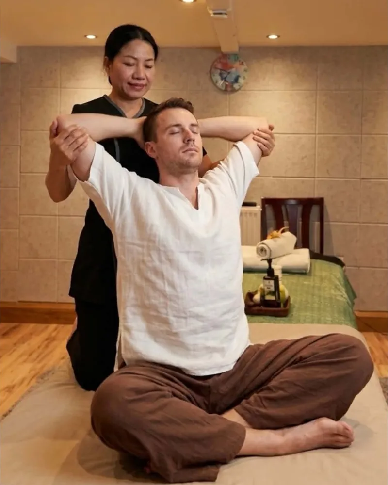 A therapist guiding a client through a seated Thai stretch